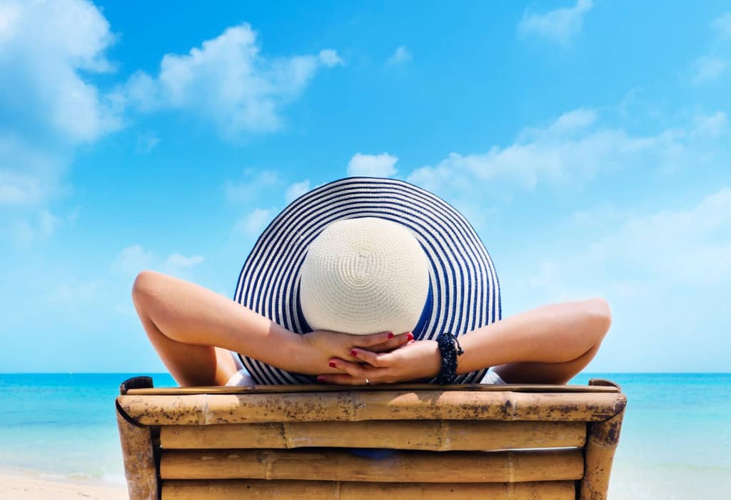 woman-in-hat-relaxing-on-beach-looking-at-sea-